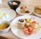 Flat lay of assorted desserts on white plates: strawberry cake, macarons, fruit tart, peaches, and a cup with paw-print cocoa.