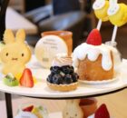 Plate of assorted desserts on a two-tier stand: bunny-shaped cookie, blueberry tart, strawberry-trosted cake with white glaze, and fresh fruit slices.