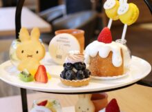 Plate of assorted desserts on a two-tier stand: bunny-shaped cookie, blueberry tart, strawberry-trosted cake with white glaze, and fresh fruit slices.