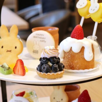Plate of assorted desserts on a two-tier stand: bunny-shaped cookie, blueberry tart, strawberry-trosted cake with white glaze, and fresh fruit slices.