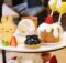 Plate of assorted desserts on a two-tier stand: bunny-shaped cookie, blueberry tart, strawberry-trosted cake with white glaze, and fresh fruit slices.