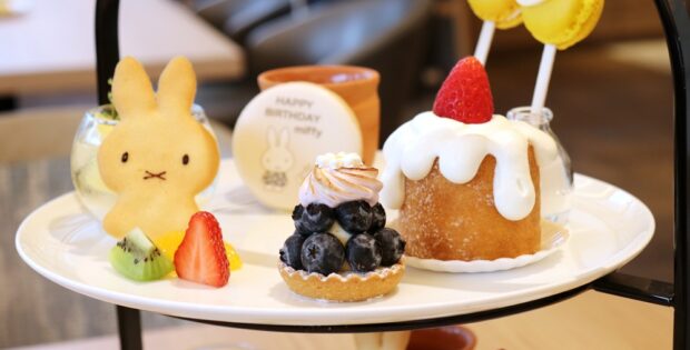 Plate of assorted desserts on a two-tier stand: bunny-shaped cookie, blueberry tart, strawberry-trosted cake with white glaze, and fresh fruit slices.