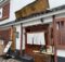 Traditional Japanese storefront with white walls, red wooden frames, white curtains, and a weathered wooden sign above the entrance.