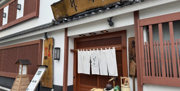 Traditional Japanese storefront with white walls, red wooden frames, white curtains, and a weathered wooden sign above the entrance.