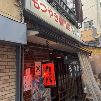 Front view of a Japanese restaurant storefront with red lanterns, posters, and fabric noren curtains outside.