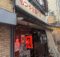 Front view of a Japanese restaurant storefront with red lanterns, posters, and fabric noren curtains outside.