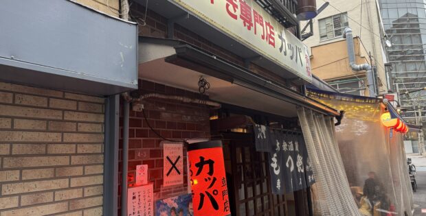Front view of a Japanese restaurant storefront with red lanterns, posters, and fabric noren curtains outside.