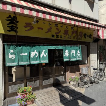 Restaurant storefront with a yellow sign, red-and-white striped awning, green text curtains, and bicycles parked outside.
