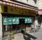 Restaurant storefront with a yellow sign, red-and-white striped awning, green text curtains, and bicycles parked outside.