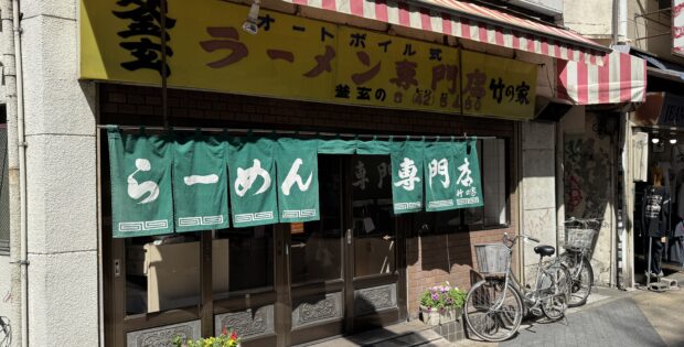 Restaurant storefront with a yellow sign, red-and-white striped awning, green text curtains, and bicycles parked outside.