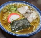 Bowl of ramen with sliced pork, green onions, fish cake, and seaweed in a savory broth