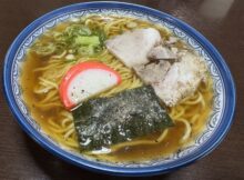 Bowl of ramen with sliced pork, green onions, fish cake, and seaweed in a savory broth