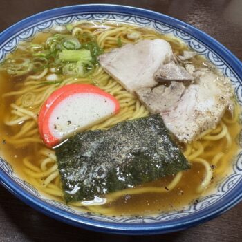 Bowl of ramen with sliced pork, green onions, fish cake, and seaweed in a savory broth