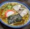 Bowl of ramen with sliced pork, green onions, fish cake, and seaweed in a savory broth