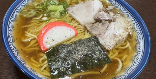 Bowl of ramen with sliced pork, green onions, fish cake, and seaweed in a savory broth