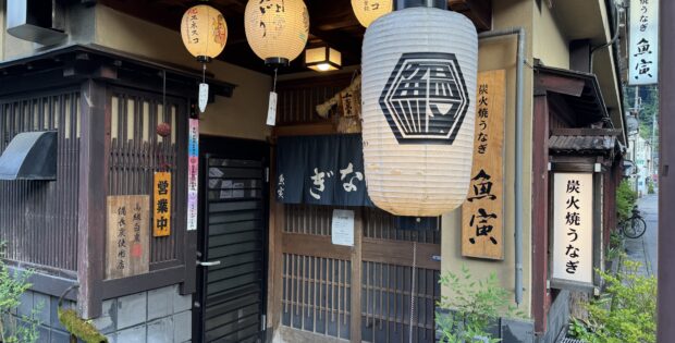 Traditional Japanese storefront with hanging lanterns and wooden lattice doors, vertical signage in Japanese on the walls.