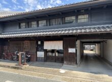 Traditional Japanese storefront with dark wooden panels, tiled roof, and noren curtains at the entrance.