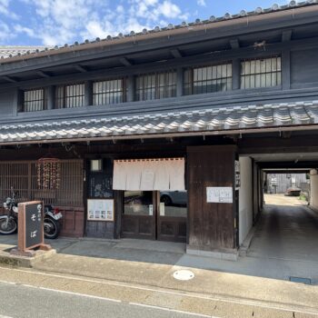 Traditional Japanese storefront with dark wooden panels, tiled roof, and noren curtains at the entrance.