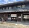 Traditional Japanese storefront with dark wooden panels, tiled roof, and noren curtains at the entrance.