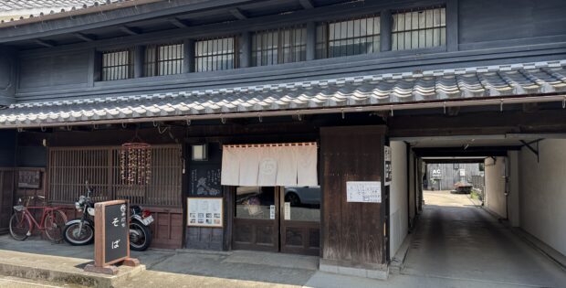 Traditional Japanese storefront with dark wooden panels, tiled roof, and noren curtains at the entrance.