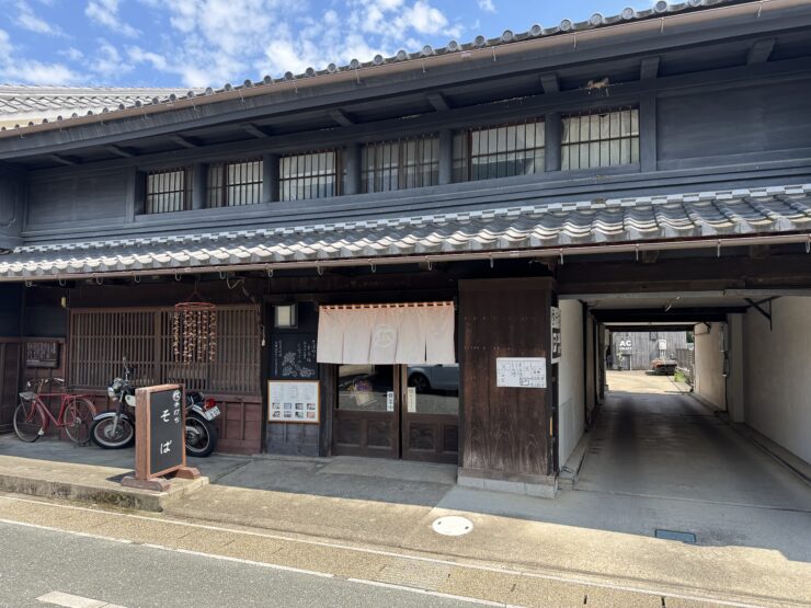Traditional Japanese storefront with dark wooden panels, tiled roof, and noren curtains at the entrance.