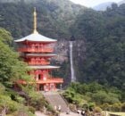 Red, three-story pagoda temple set in a lush green valley with a waterfall in the background.