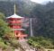 Red, three-story pagoda temple set in a lush green valley with a waterfall in the background.