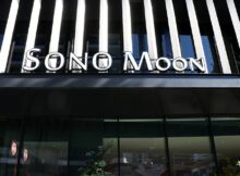 Storefront facade with bold, white 'SONO MOON' signage above large glass doors and striped architectural panels behind.
